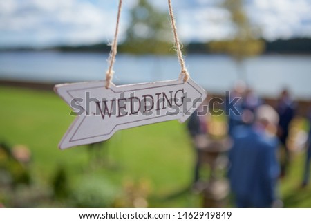 A wooden direction with wedding text is hanging near location of the ceremony, selective focus