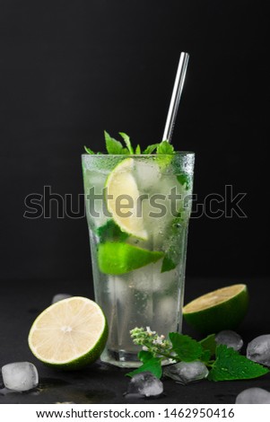 Cocktail Mojito with ice in a glass, lime, leaf mint and metal straw  on a dark background