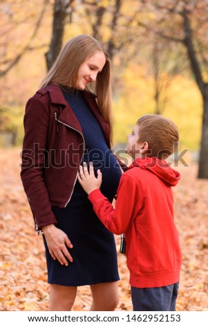Boy hugging belly of his pregnant mother. Look into each other's eyes. Autumn park on the background