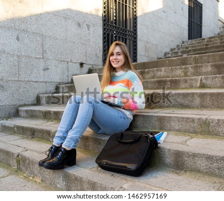 Attractive trendy teen student or young college girl working on laptop on the internet, blogging, chatting and checking email on steps in a european city. In Student learning online City lifestyle.