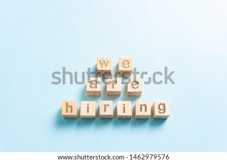 "We are hiring" banner in the middle, all this on small wood cubes on paper with blue background and copy space. Job concept.