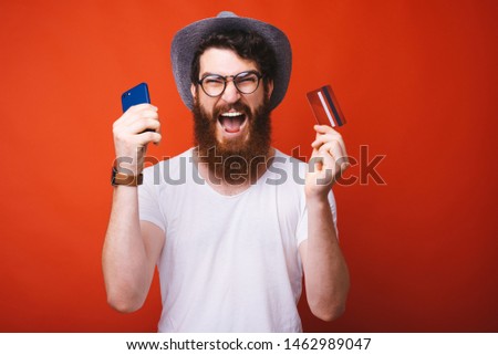 Photo of amazed man holding smartphone and credit card, shopping onlie concept