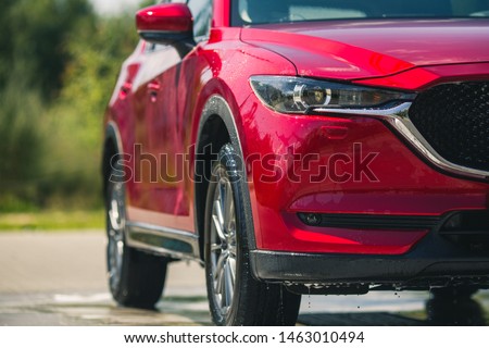 Red car with white soap on the body in car care shop. Isolated on  background. Manual car wash with pressurized water in car wash outside.