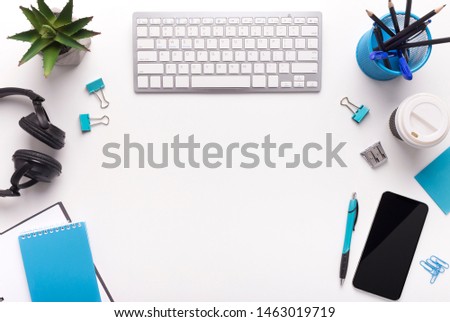 Office table with plants, keyboard, cellphone with blank screen and blue colored supplies on white, copy space