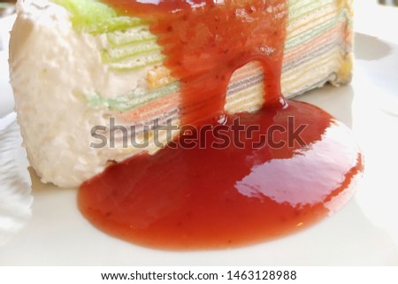 Colorful Rainbow Crepes Cake with Berry Sauce in white plate on wooden table background with copy space.