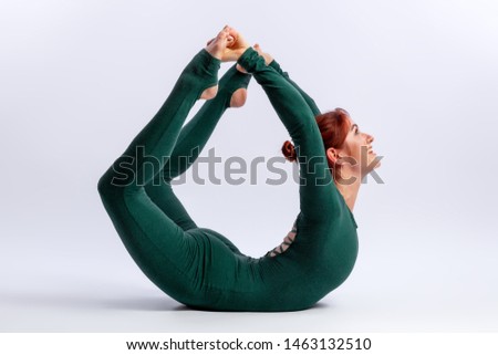 Beautiful slim woman in sports overalls  doing yoga, standing in an asana balancing  bow pose in a difficult position for flexibility  on white  isolated background. The concept of sports