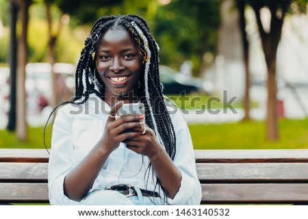 Portrait of a young African American girl with pigtails . The girl is talking on a mobile phone, smiling. Sunny day. Outdoor photo.