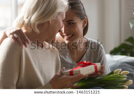 Close up grown up loving daughter congratulates eight march or international women day middle aged mother giving her gift box spring flowers white tulips, life events, attention love and care concept