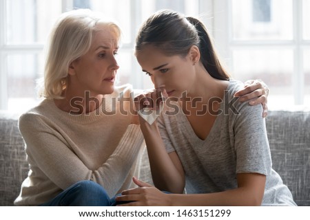 Loving mid aged mother and grown up daughter sit on couch, worried parent calms adult child with broken heart first love helps her survive bad divorce break up with boyfriend, care and support concept Royalty-Free Stock Photo #1463151299