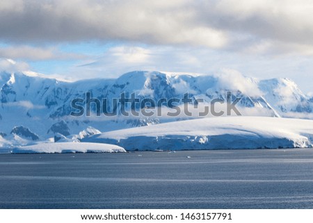 Soft sunset lights on snow-capped mountains and icy shores in the Antarctic Peninsula, Antarctica