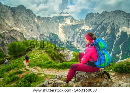 Active hiking woman with colorful backpack. Hiker woman relaxing and enjoying the view with Jalovec mountain peak, from the Slemenova Spica hiking place, Julian Alps, Slovenia, Europe Royalty-Free Stock Photo #1463168039