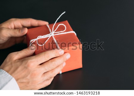 Corporate birthday party. Closeup of red paper wrapped gift box in man hands. Copy space.