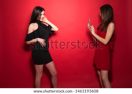 Happy woman taking picture of her friend using phone over red background