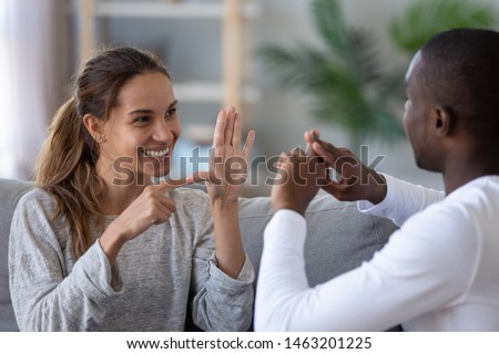 Smiling mixed ethnicity couple or interracial friends talking with sign finger hand language, happy two deaf and mute hearing impaired people communicating at home sit on sofa showing hand gestures Royalty-Free Stock Photo #1463201225