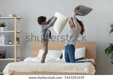 Funny happy african mixed race ethnicity family mum and little cute son having fun pillow fight on bed, young mother laughing playing funny game enjoy leisure activity with small child boy in bedroom Royalty-Free Stock Photo #1463201639