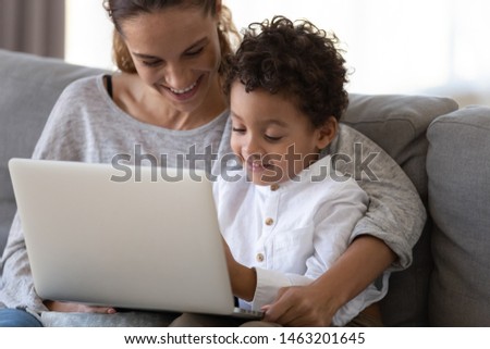 Happy family loving mixed race mother baby sitter embrace african american cute little kid child son learning using laptop computer watching cartoons shopping online on website hold notebook at home