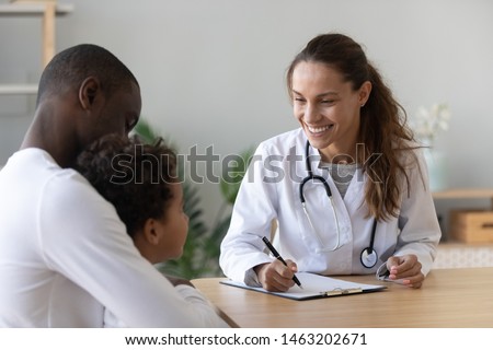 Smiling female doctor listen consult cute african boy make notes in patient card at medical checkup appointment, black dad and child son visit pediatrician talk in clinic, children healthcare concept Royalty-Free Stock Photo #1463202671