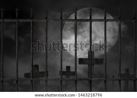 Scary background cemetery cross and graveyard fence with dark silhouette in large moon, concept of horror and Halloween