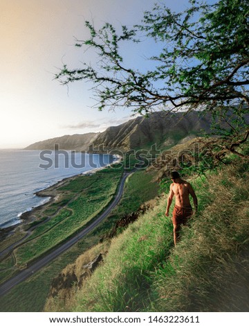 A male walking on a steep green hill with the beautiful sea and hills in the background