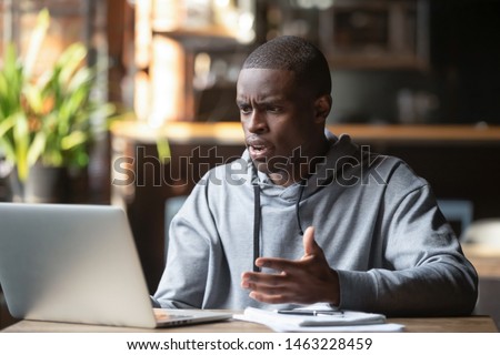 Frustrated black male student work at laptop get mad having device software operational problems, angry african American guy man feel confused with slow internet connection on computer or virus attack Royalty-Free Stock Photo #1463228459