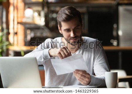 Focused man sitting in cafe working on laptop drinking coffee open post envelop get message from college, concentrated male student receive reply from university unwrap letter correspondence Royalty-Free Stock Photo #1463229365