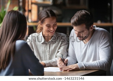 Excited millennial couple meeting with female realtor or broker in cafe sign contract buying first property together, happy spouses put signature on agreement close deal with banker take loan Royalty-Free Stock Photo #1463231546