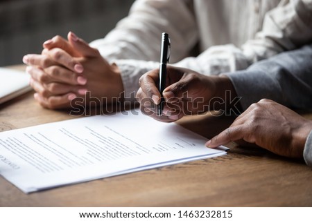 Close up of african American husband put signature on contract buying first house with wife, multiracial couple sign agreement closing deal with realtor or banker, taking property loan or mortgage