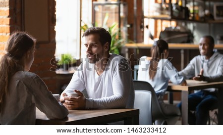 Millennial couple sit at cafe table drinking hot coffee talking discussing things, diverse young men and women meeting in coffeehouse speaking get acquainted taking part in speed dating. Love concept Royalty-Free Stock Photo #1463233412