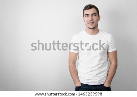 Authentic portrait of caucasian smiling young man in white blank t-shirt with copy space on grey background