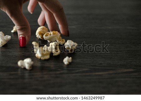 female Hand takes popcorn on wood table. creative background. Top view.