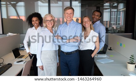 Smiling multiethnic team with Caucasian male leader forefront look at camera posing for group picture at workplace, motivated diverse colleagues make photo together showing unity and support