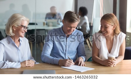 Happy husband put signature on contract buy first house from realtor together with excited young wife, overjoyed couple tae loan sign agreement after successful meeting with female banker or realtor Royalty-Free Stock Photo #1463265032
