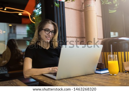 Happy smiling woman in glasses skilled freelance worker having online training course via laptop computer while sitting in coffee shop outdoors. Cheerful female blogger using applications on notebook 