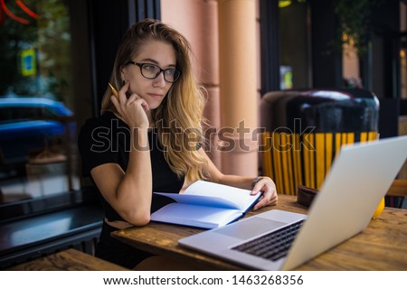 Thoughtful woman with pensive look in spectacles skilled real estate analyst reading information on website via laptop computer, sitting in coffee shop. Pondering female having online training course 