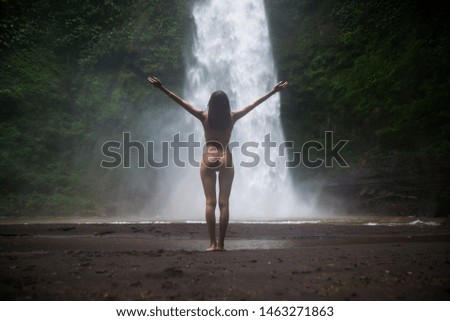 Beautiful young woman posing at the great Sekumpul waterfall in the deep rainforest of Bali island, Indonesia.