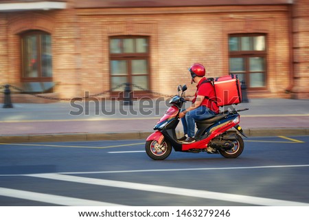Delivery boy of takeaway on scooter with isothermal food case box driving fast. Express food delivery service from cafes and restaurants. Courier on the moto scooter delivering food. Royalty-Free Stock Photo #1463279246