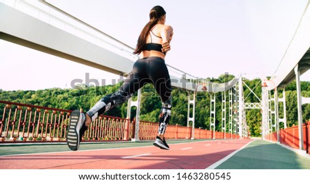 Faster than wind. Back view full length photo of jogging young sporty woman on city bridge.