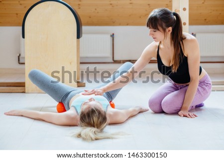 Female instructor helping for client doing self-massage technique applying special balls for back pain relief, working out lying on floor at pilates studio.Correct posture maintaining body concept.