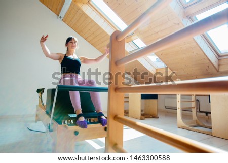 Healthy positive brunette woman in black top sportswear professional instructor pilates practicing plank, press, stretching exercise on reformer bed in pilates studio.
