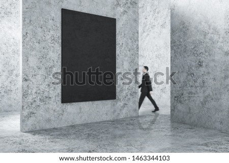 Businessman walking in concrete interior with empty frame on wall. Gallery concept. Mock up,