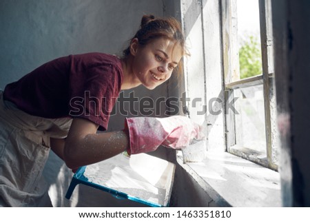 young woman paints the wall in the house interior