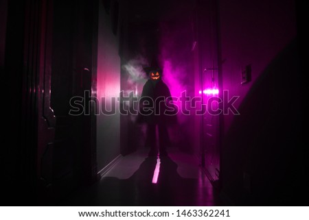 Halloween concept. Creepy silhouette in the dark corridor with pumpkin head. Toned light with fog on background.