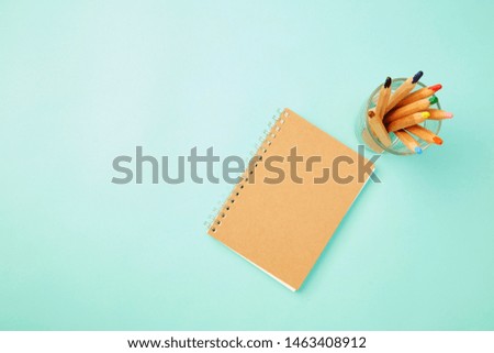 Flat lay photo, Colorful Crayon in glass With a notebook on pastel pale blue background, World Teachers' Day or Back to school concept , copy space for text