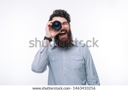 Photo of funny bearded man in casual covering his eye with lens