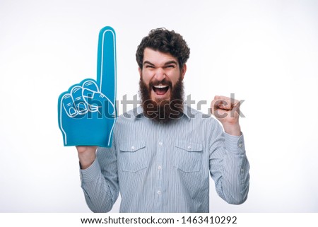 Portrait of a cheerful excited  man with a foam finger shouting and looking at camera  Royalty-Free Stock Photo #1463410292