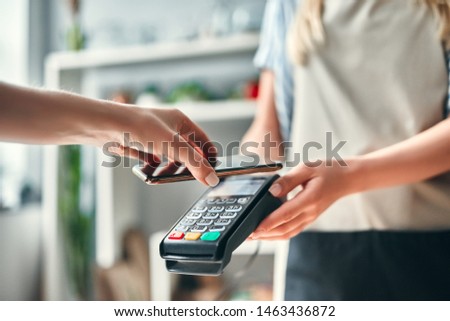 Female florist in flower shop. Young beautiful blonde selling flowers and succulents. Cropped image of customer paying using smart phone. Royalty-Free Stock Photo #1463436872
