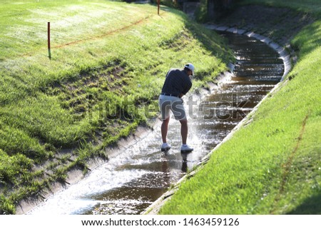 A golfer playing in a tournament, hits a shot from a small creek