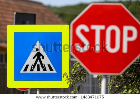 Stop and pedestrian crossing sign one next to another on a street