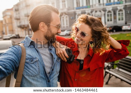 attractive smiling man and woman traveling together, stylish couple in love taking selfie photos on phone on romantic trip, sunny summer city, wearing shirt, sunglasses, travelers having fun