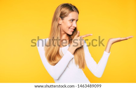 Modern stuff. Happy beautiful blonde woman is pointing on her palm isolated on yellow